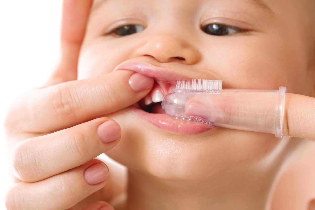 A baby’s first teeth being cleaned with a soft silicone finger brush