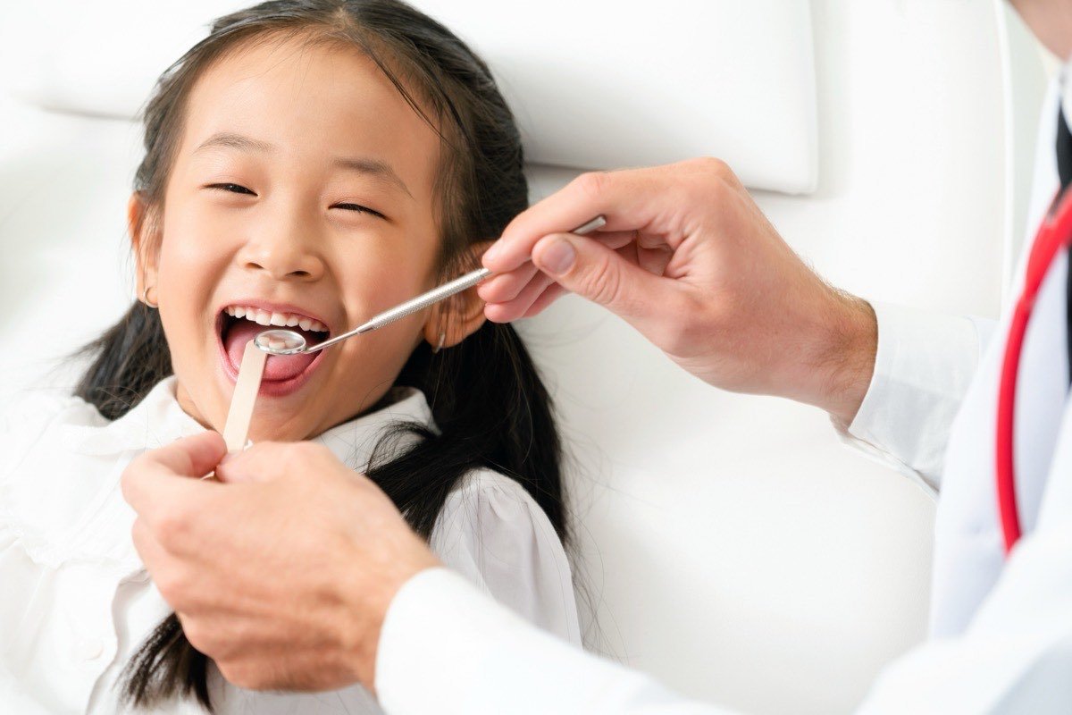 A young girl laughing during a dental check-up while the dentist examines her teeth with a mouth mirror