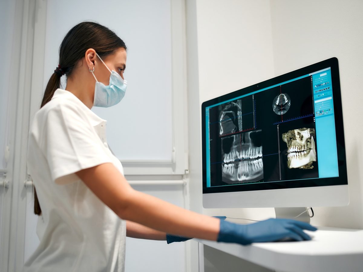 A dental clinician reviewing 3D CBCT and panoramic X-ray images on a medical-grade DICOM monitor