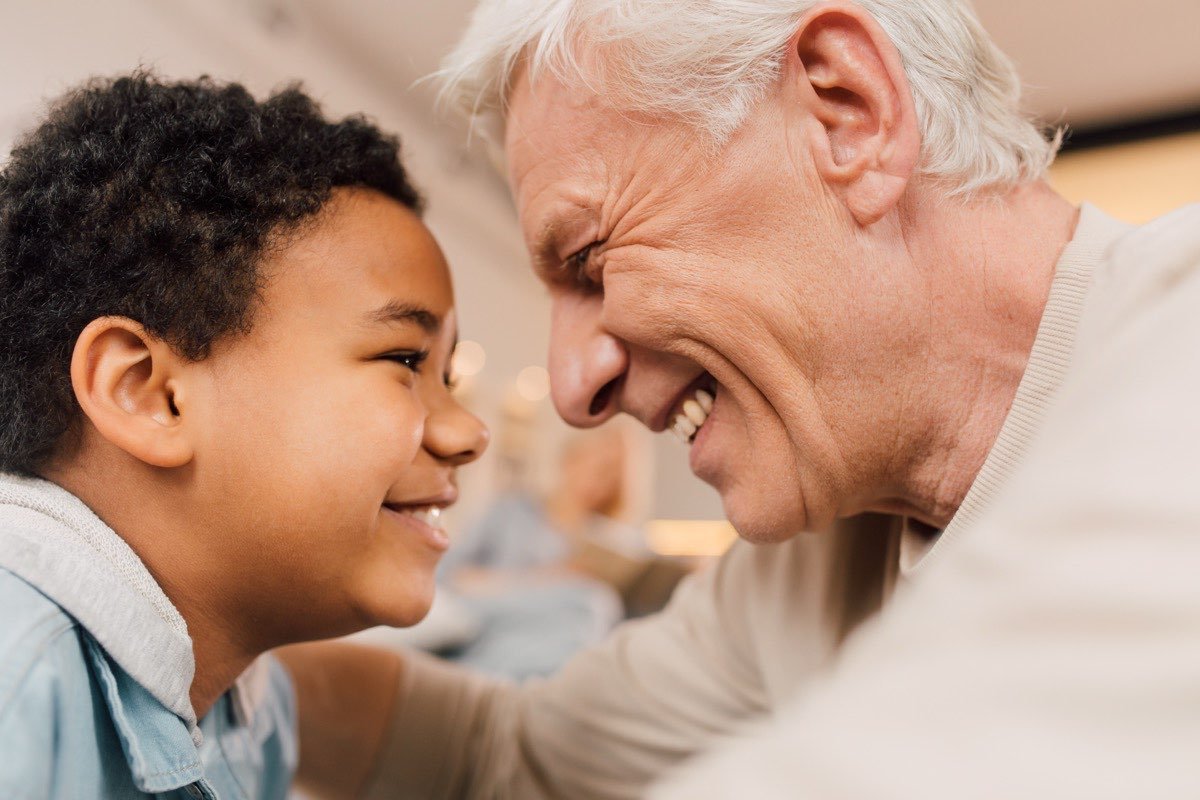 A grandfather and his young grandson laughing together face to face