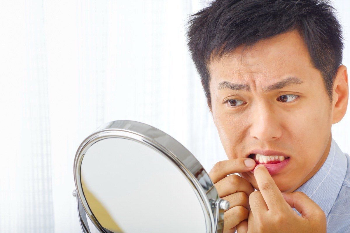 A man examining his gums closely in a hand mirror, checking for redness along the gumline