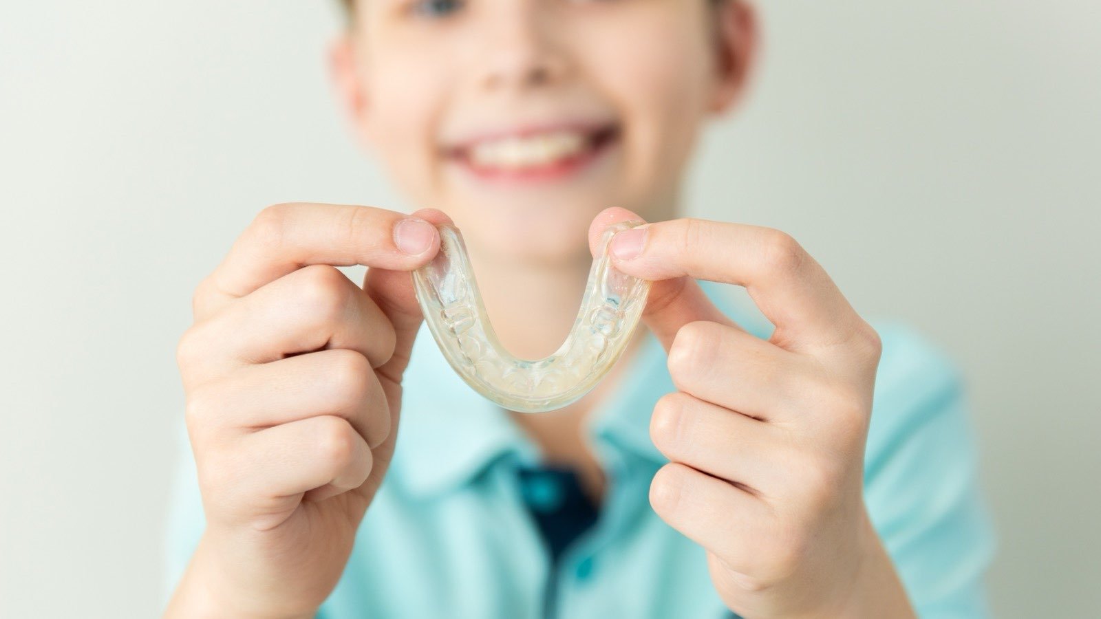 A smiling boy holding up a clear orthodontic aligner tray